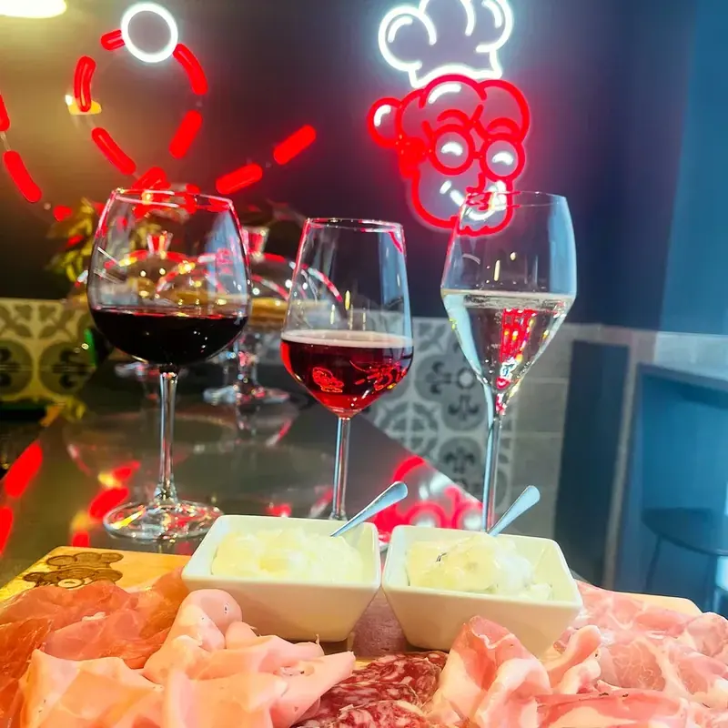 Tre calici, rosso, rosato e bollicine, davanti al neon della Nonna e a un tagliere