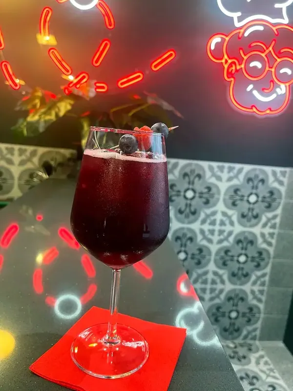 A glass of red with berries under Nonna’s neon sign
