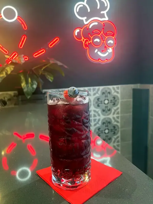A dark highball with berries and the neon lights