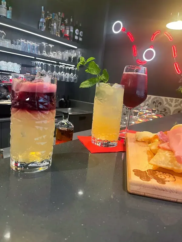 Three cocktails in a row on the counter, with the board and the bar bottles behind