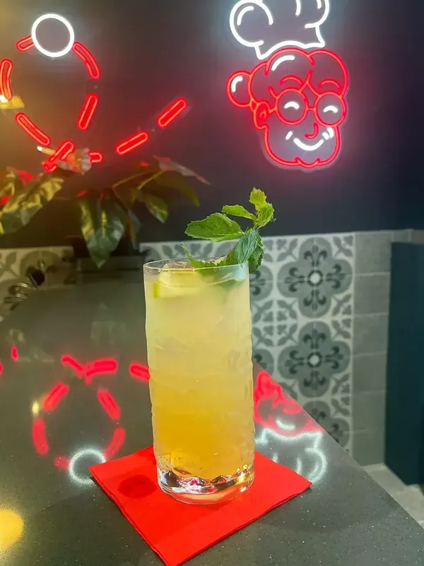 Un long drink giallo con la menta davanti al neon della Nonna