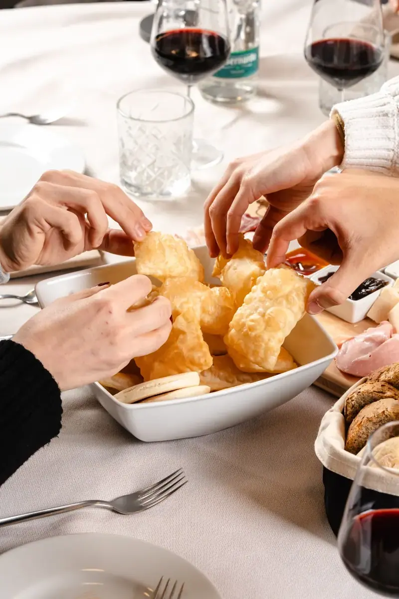 Mani che prendono il gnocco fritto caldo, con un calice di rosso