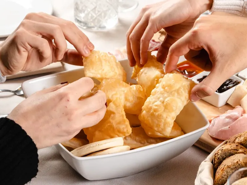 Hands reaching for hot gnocco fritto, with a glass of red