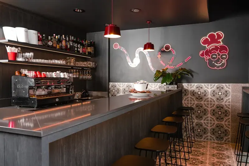 Il bancone del bar di Nonna Emilia, con le lampade rosse e il ritratto al neon