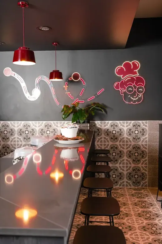 Il bar con il ritratto al neon della Nonna, gli sgabelli e le lampade rosse