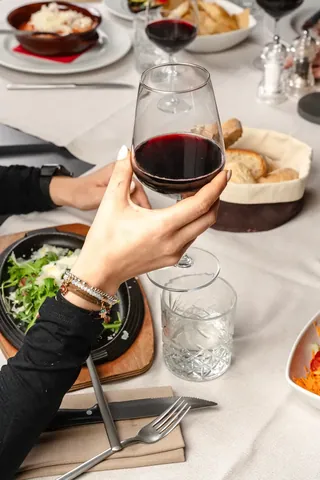 Un calice di vino rosso sopra la tovaglia bianca, accanto ai piatti