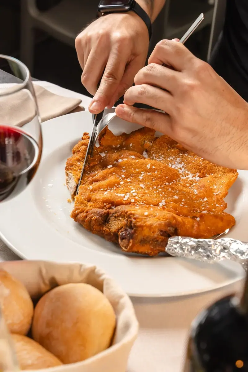 La Milanese col manico tagliata a tavola, con il pane e un calice di rosso